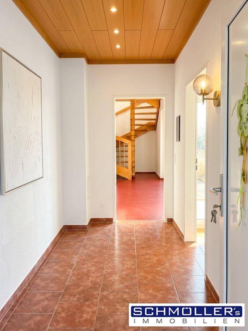 Heller Flur mit Terrakotta-Fliesenboden und Holzdecke, der zu einer Wendeltreppe führt.