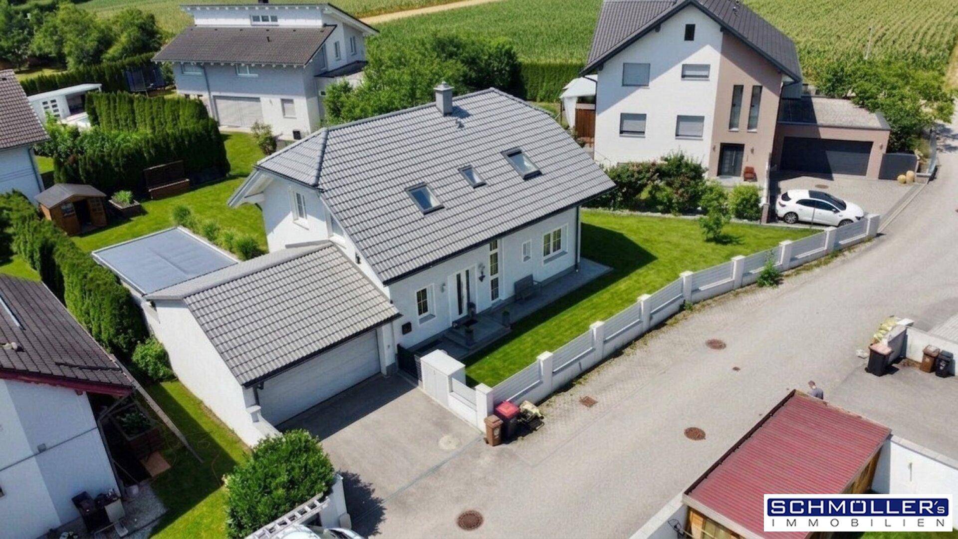 Luftaufnahme eines modernen Einfamilienhauses mit Garage, Vorgarten und gepflegter Umgebung.