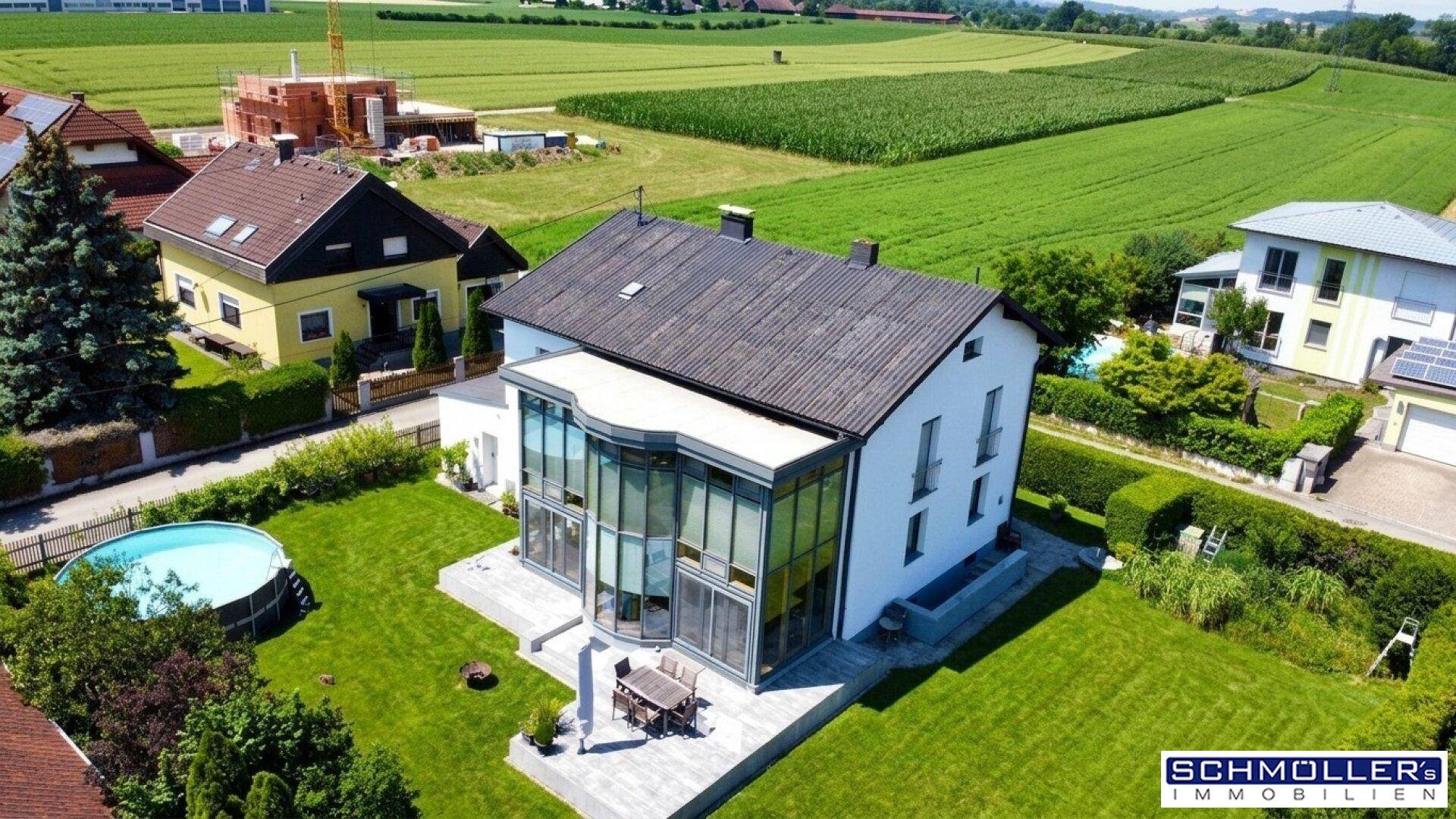 Übersicht des Anwesens mit großem Garten, Pool und moderner Glaserweiterung unter blauem Himmel.