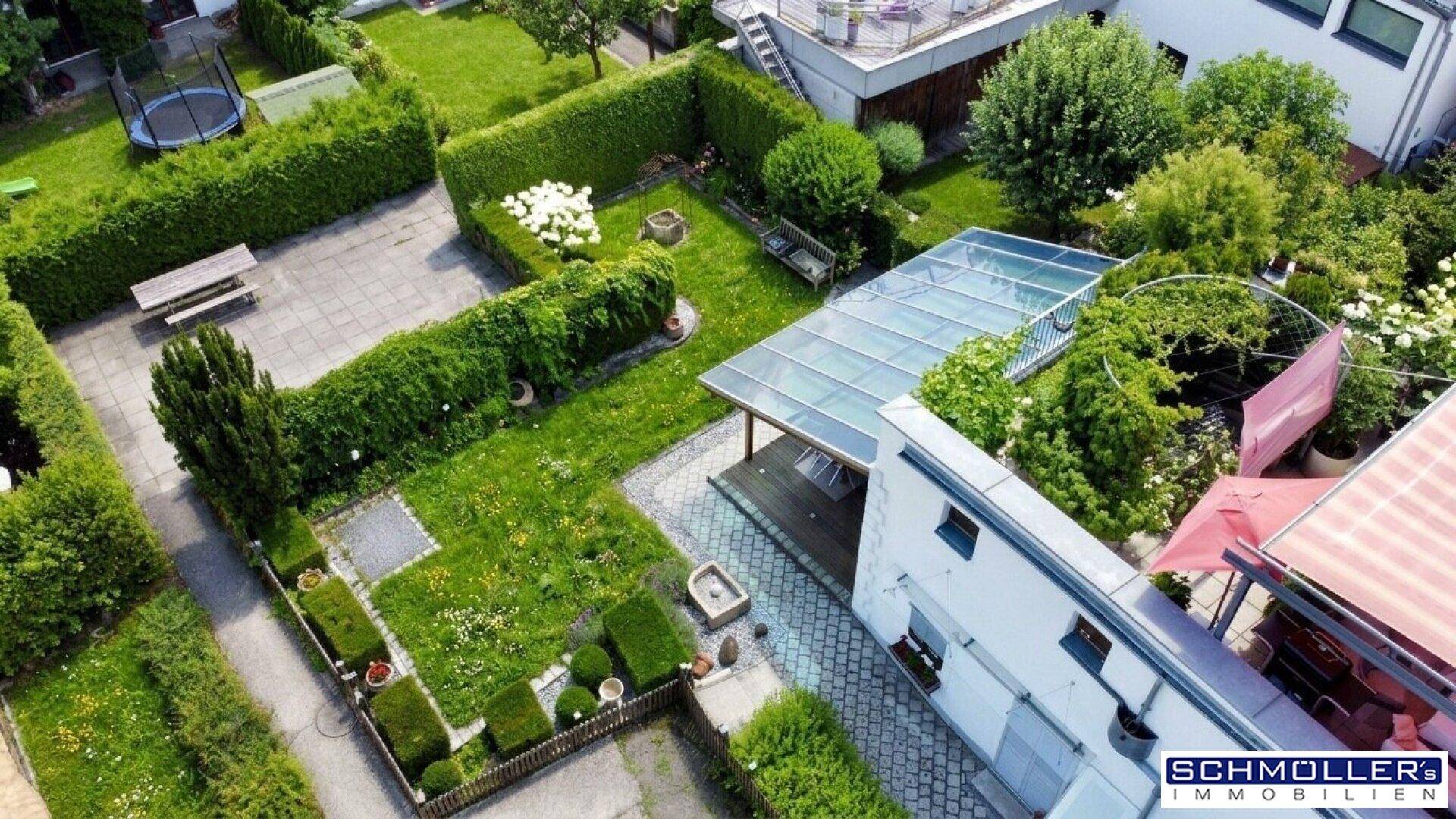 Luftaufnahme eines gepflegten Gartens mit Rasenflächen, hohen Hecken, einer überdachten Terrasse und einem Trampolin.