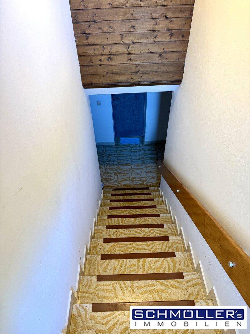 Treppenhaus mit Holzdecke und gemusterten Stufen, das in einen unteren Bereich führt.