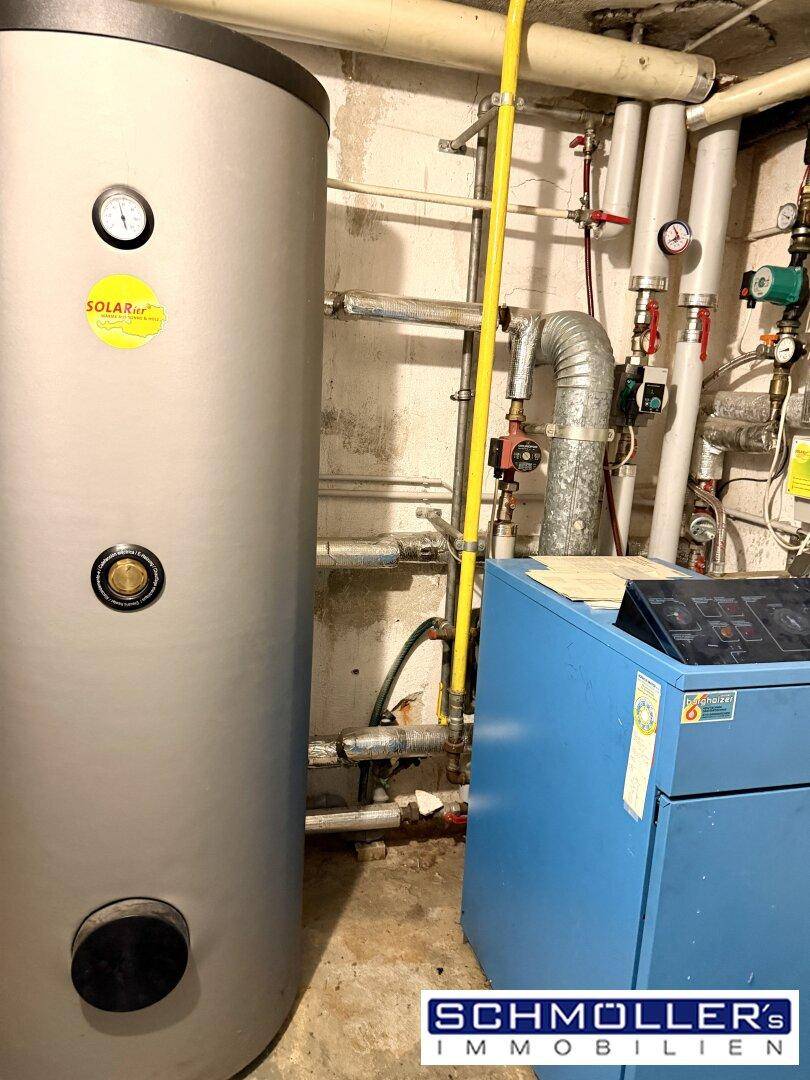 Heizungsraum mit Warmwasserspeicher und Heizungsanlage, umgeben von Rohren und Leitungen.