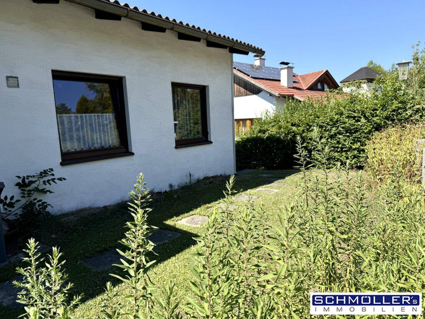 Seitenansicht des Hauses mit einem kleinen Rasenbereich und Pflanzen im Vordergrund.