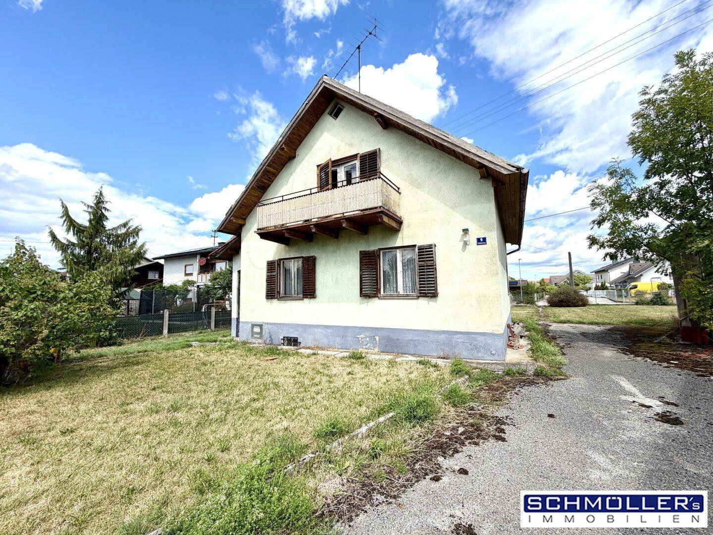 Seitenansicht des Hauses mit kleinem Holzbalkon und einem unbefestigten Weg im Vorgartenbereich.