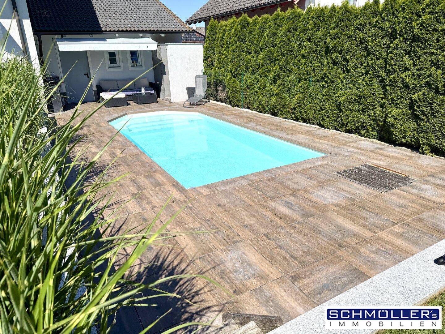 Gepflegter Außenbereich mit großem Pool, umgeben von einer Terrasse und grüner Hecke.