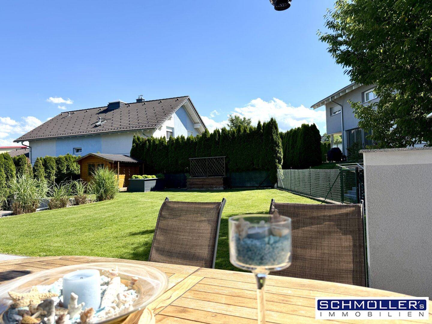 Sonniger Garten mit Rasenfläche, Hecke und gemütlichem Essbereich im Freien.