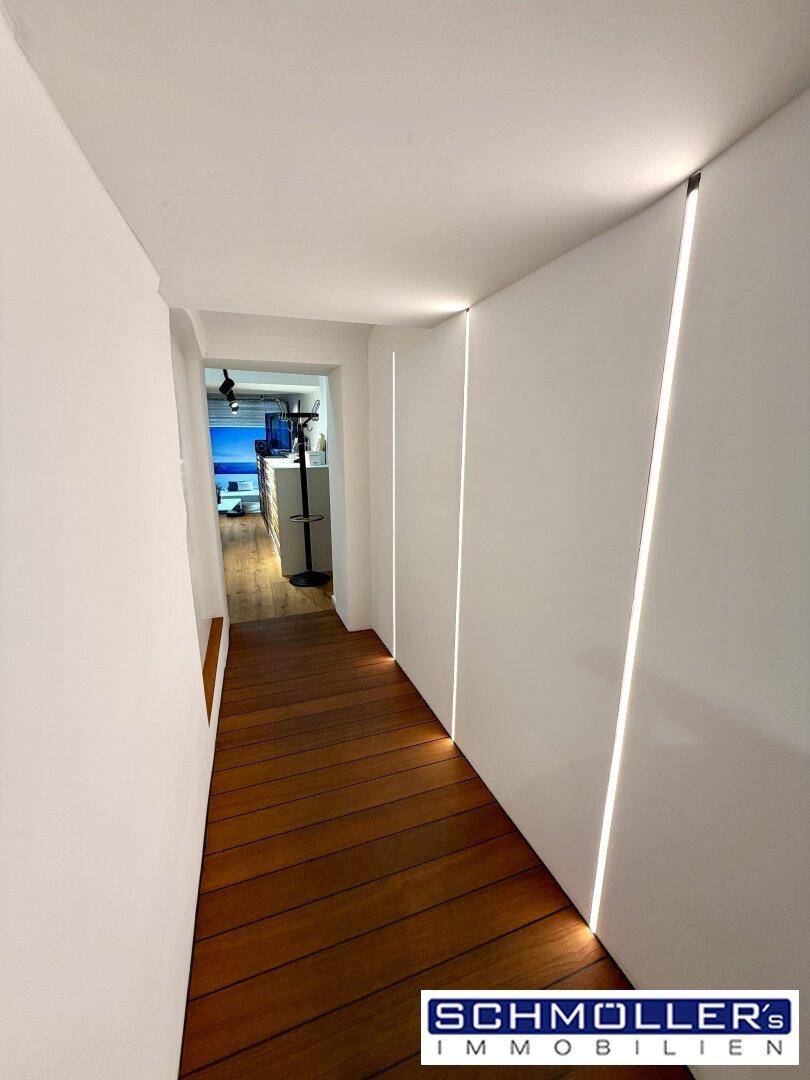 Moderner Flur mit Holzplankenboden und integrierter LED-Beleuchtung an den Wänden, sehr einladend.