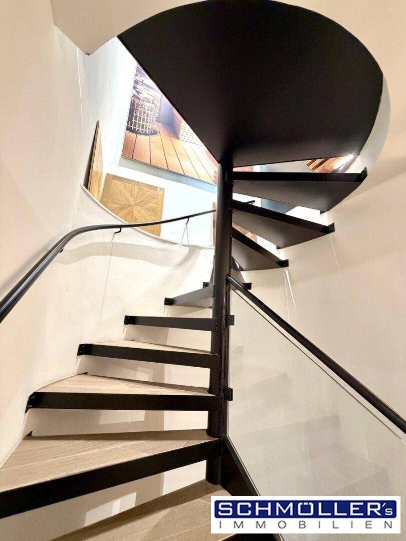 Elegante schwarze Wendeltreppe mit Glasgeländer und Holzstufen, die verschiedene Ebenen verbindet.