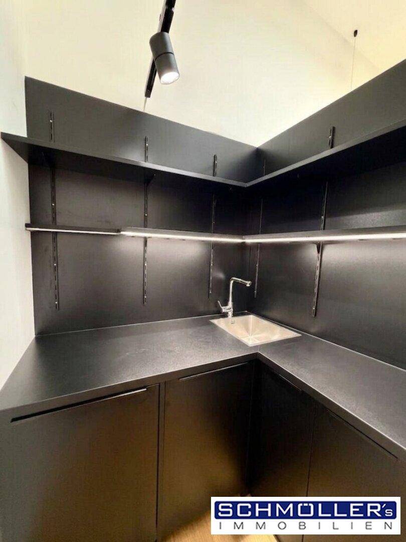 Funktionale, moderne Küchenzeile in Schwarz mit Spülbecken und offenen Regalen, sehr platzsparend.