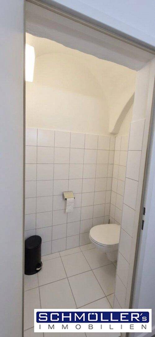 Helle Gästetoilette mit weißen Fliesen, Wand-WC und gewölbter Decke, sauber und funktional.
