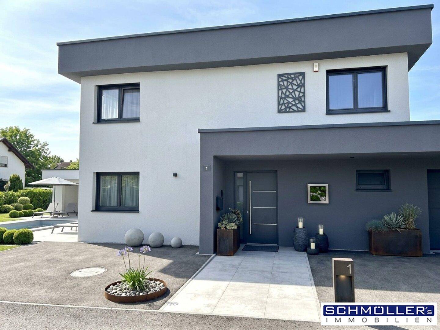 Moderne Hausfassade in Weiß und Grau mit gepflegtem Vorgarten und Einfahrt.