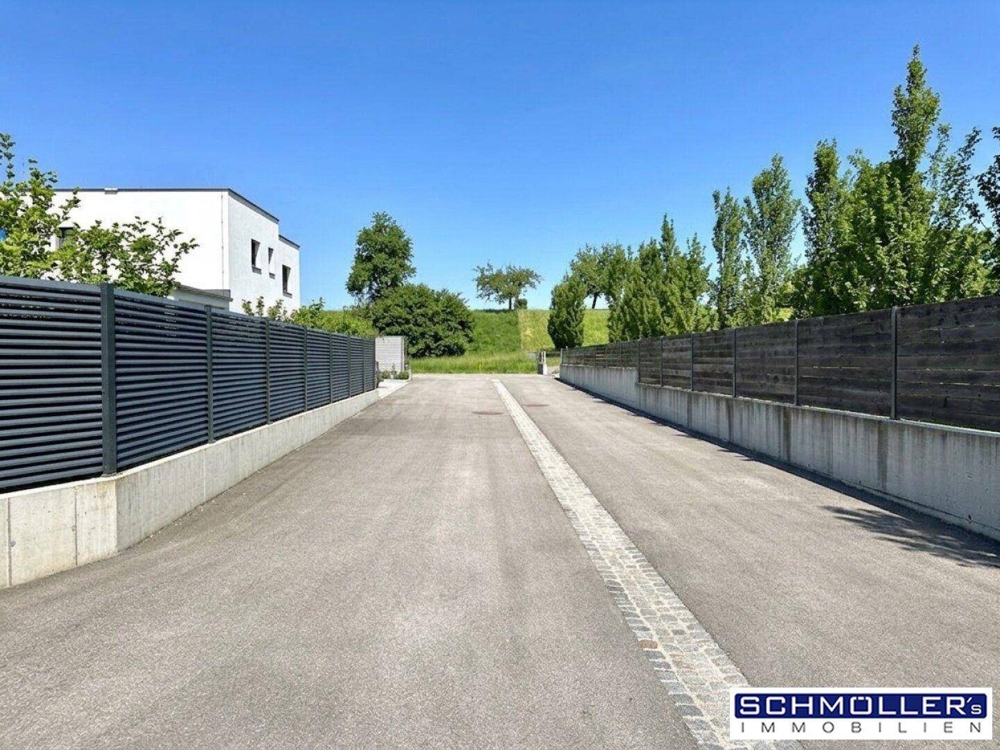 Zufahrtsweg zum Anwesen, umgeben von Zäunen und grüner Landschaft unter blauem Himmel.