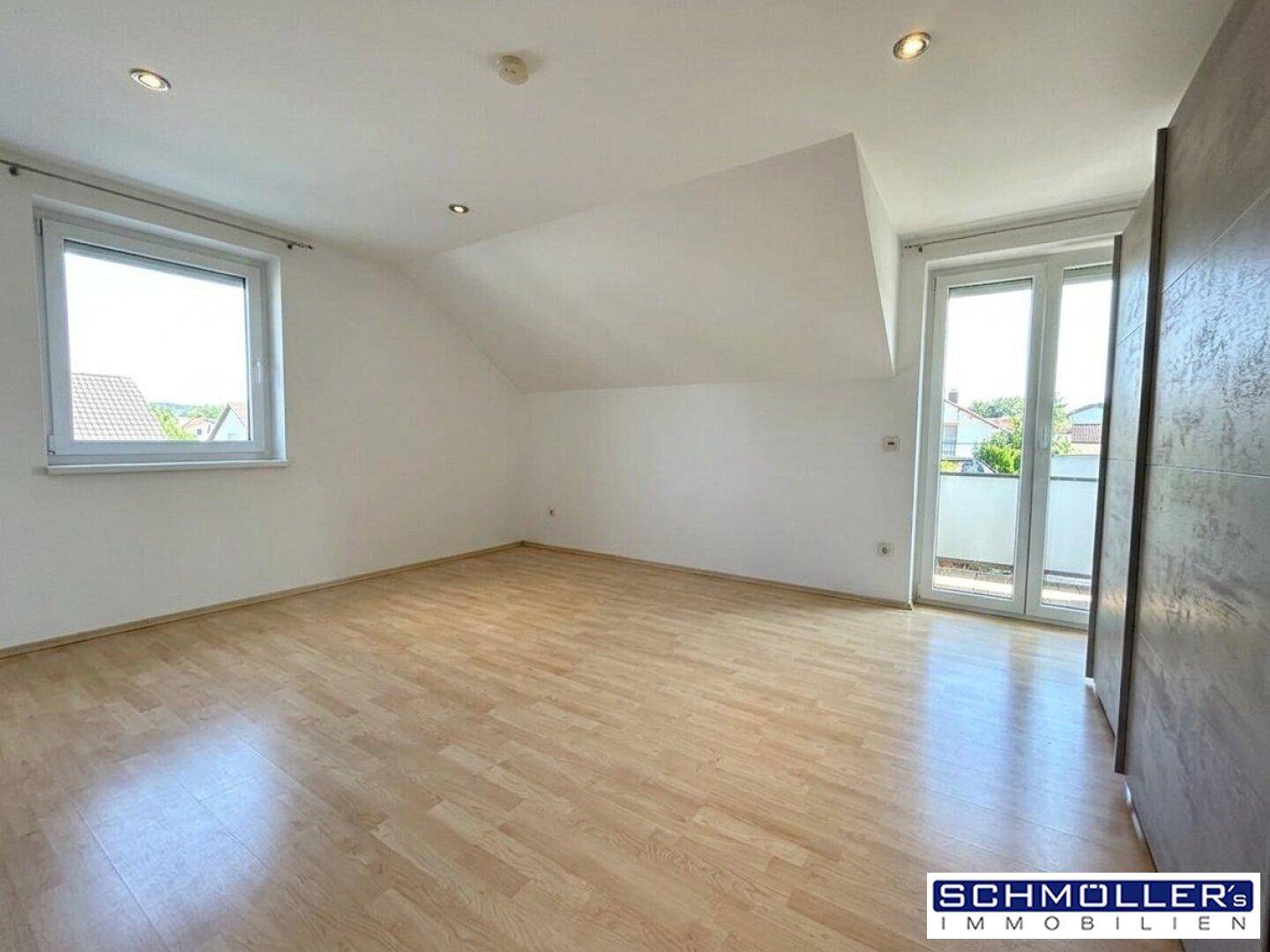 Lichtdurchfluteter Dachgeschossraum mit Laminatboden, schrägen Wänden und Zugang zu einem Balkon.