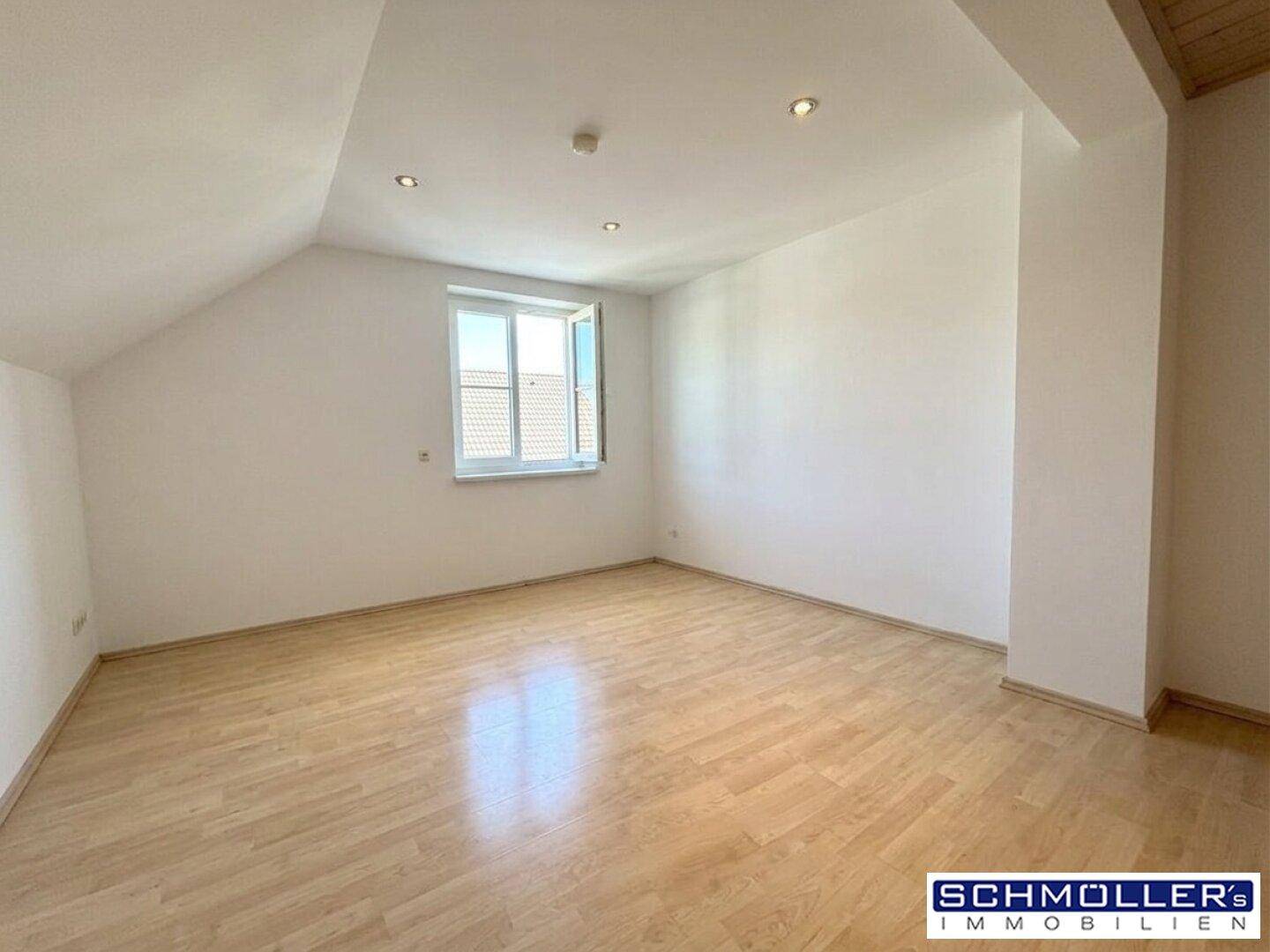 Heller, leerer Raum im Dachgeschoss mit schrägen Wänden, Laminatboden und einem Fenster.