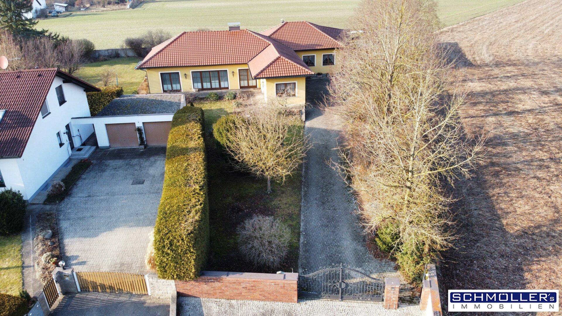 Luftaufnahme eines Einfamilienhauses mit Zufahrt, Vorgarten und angrenzenden Feldern.