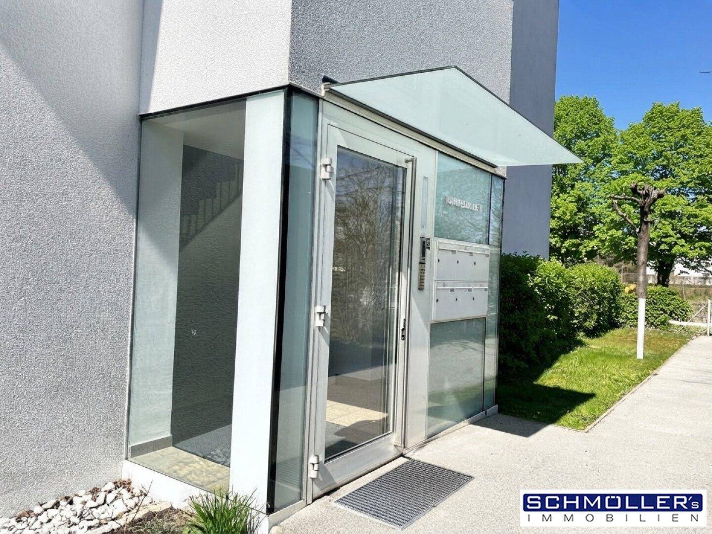 Moderner Eingangsbereich des Gebäudes mit Glasfassade und Briefkästen.