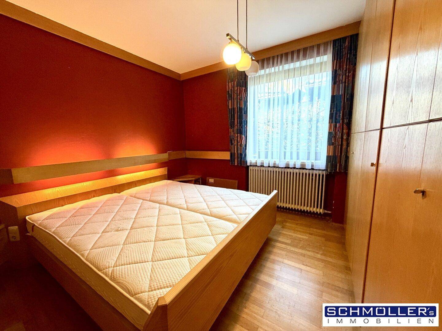 Schlafzimmer mit Doppelbett, Holzfußboden und roten Wänden, die eine gemütliche Atmosphäre schaffen.