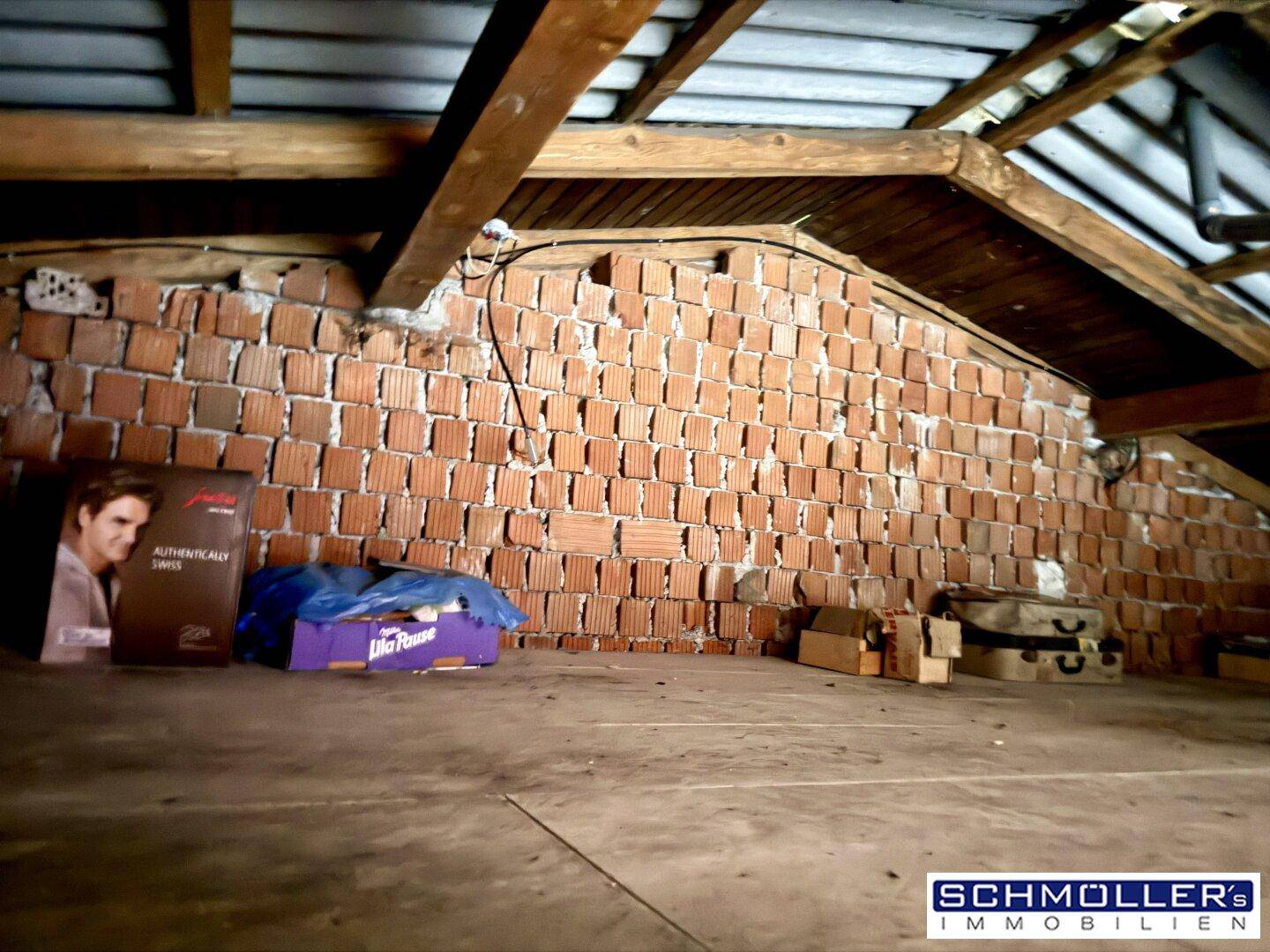 Unausgebauter Dachboden mit sichtbaren Holzbalken und Ziegelwänden, ideal als Stauraum.