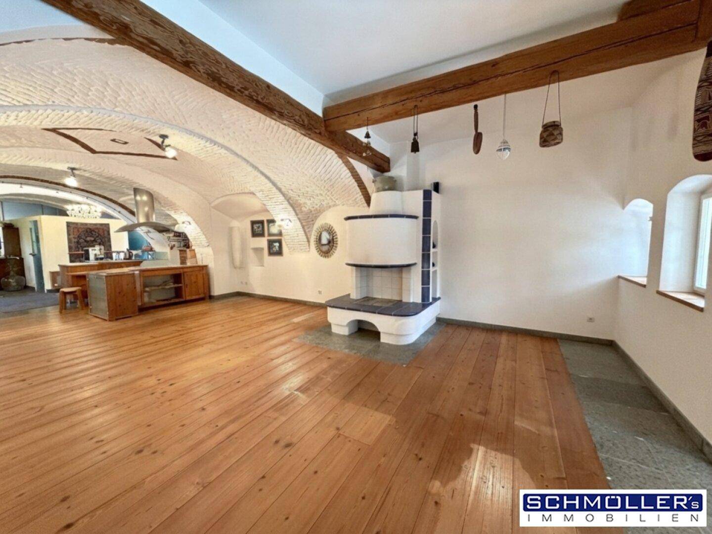 Großzügiger Wohnbereich mit Holzboden, sichtbaren Holzbalken und einem traditionellen Kachelofen.