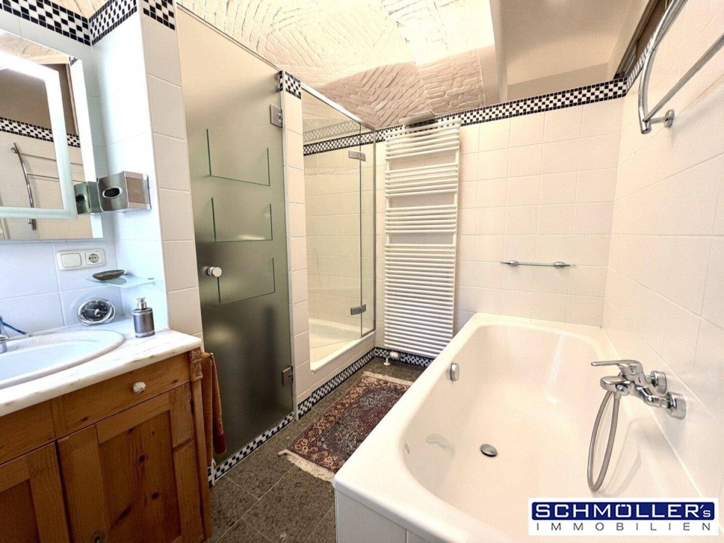 Modernes Badezimmer mit Badewanne, Duschkabine, beheiztem Handtuchhalter und Steinboden.