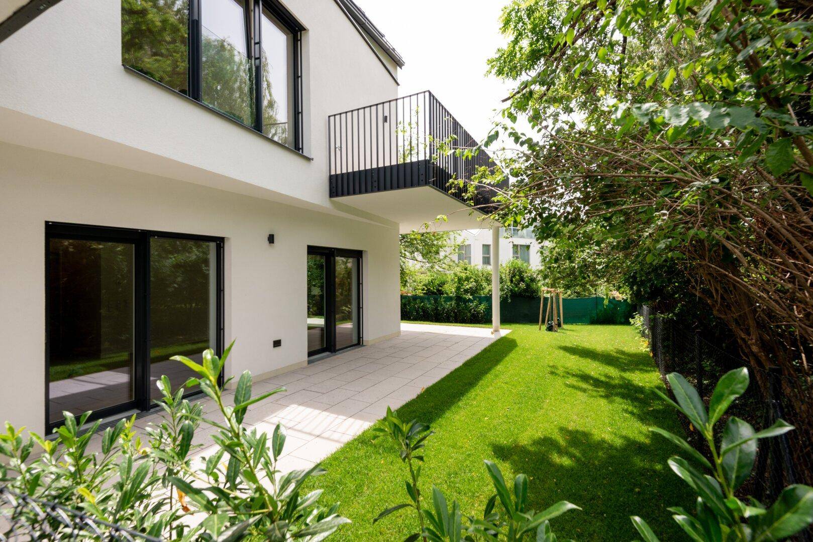 Ebenerdige Terrasse mit Steinplatten und Rasenfläche, direktem Zugang zum Garten und kleinem Balkon.