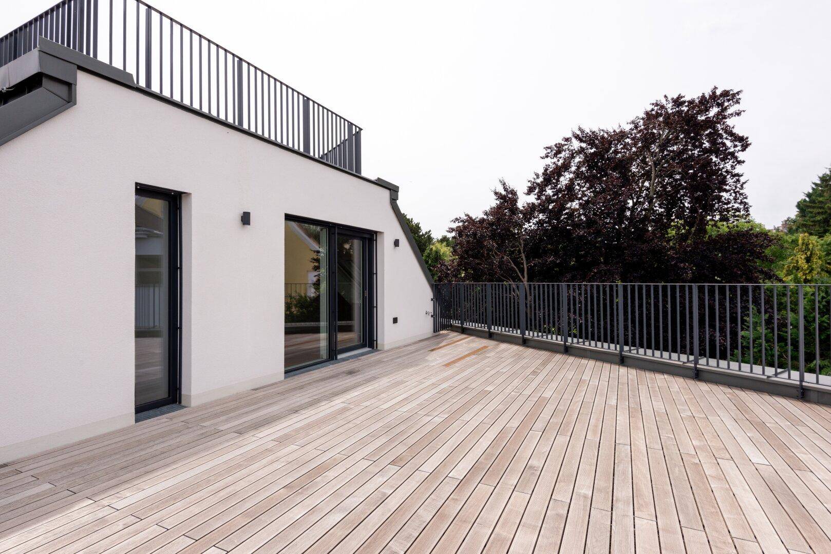 Geräumige Dachterrasse mit Holzbelag, schwarzen Geländern und Blick ins Grüne.