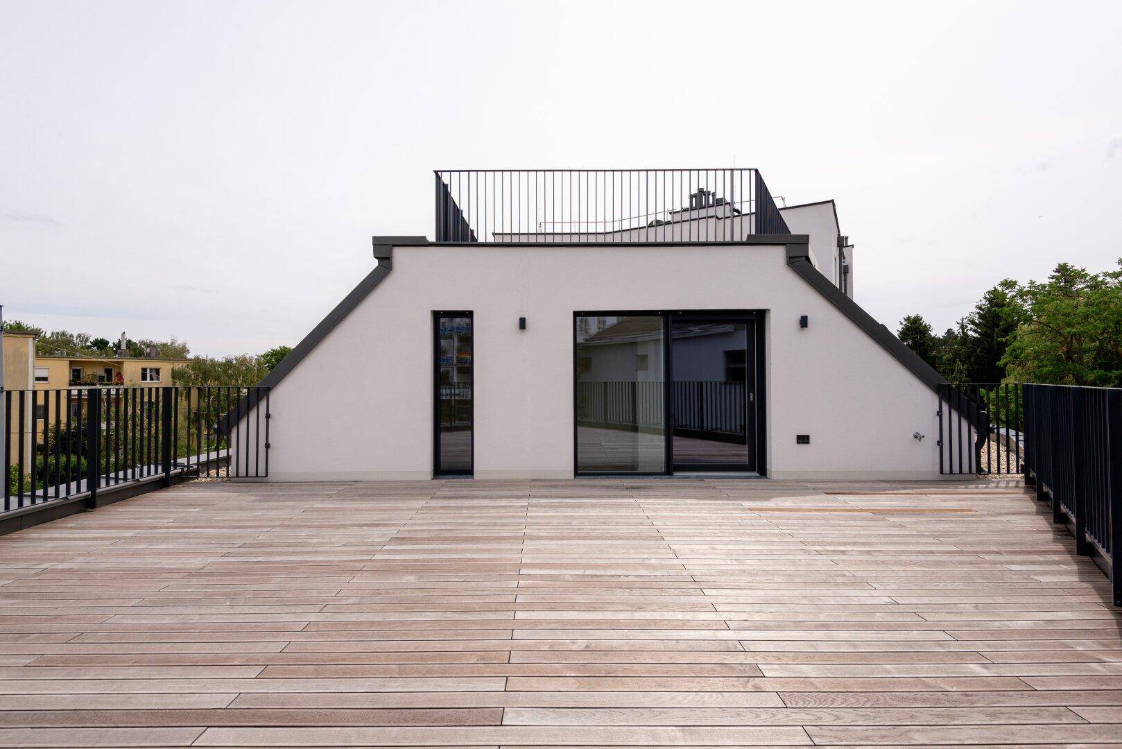 Weitläufige Dachterrasse mit Holzplanken und moderner weißer Fassade unter bewölktem Himmel.