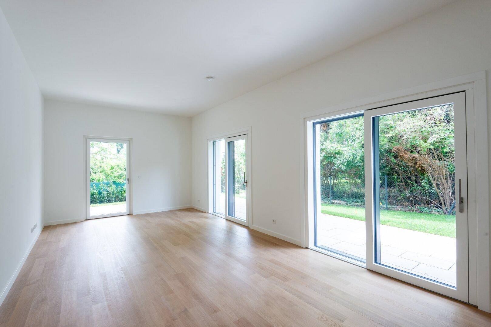Geräumiger Wohnraum mit hellem Holzparkett und großen Schiebetüren zum Garten.
