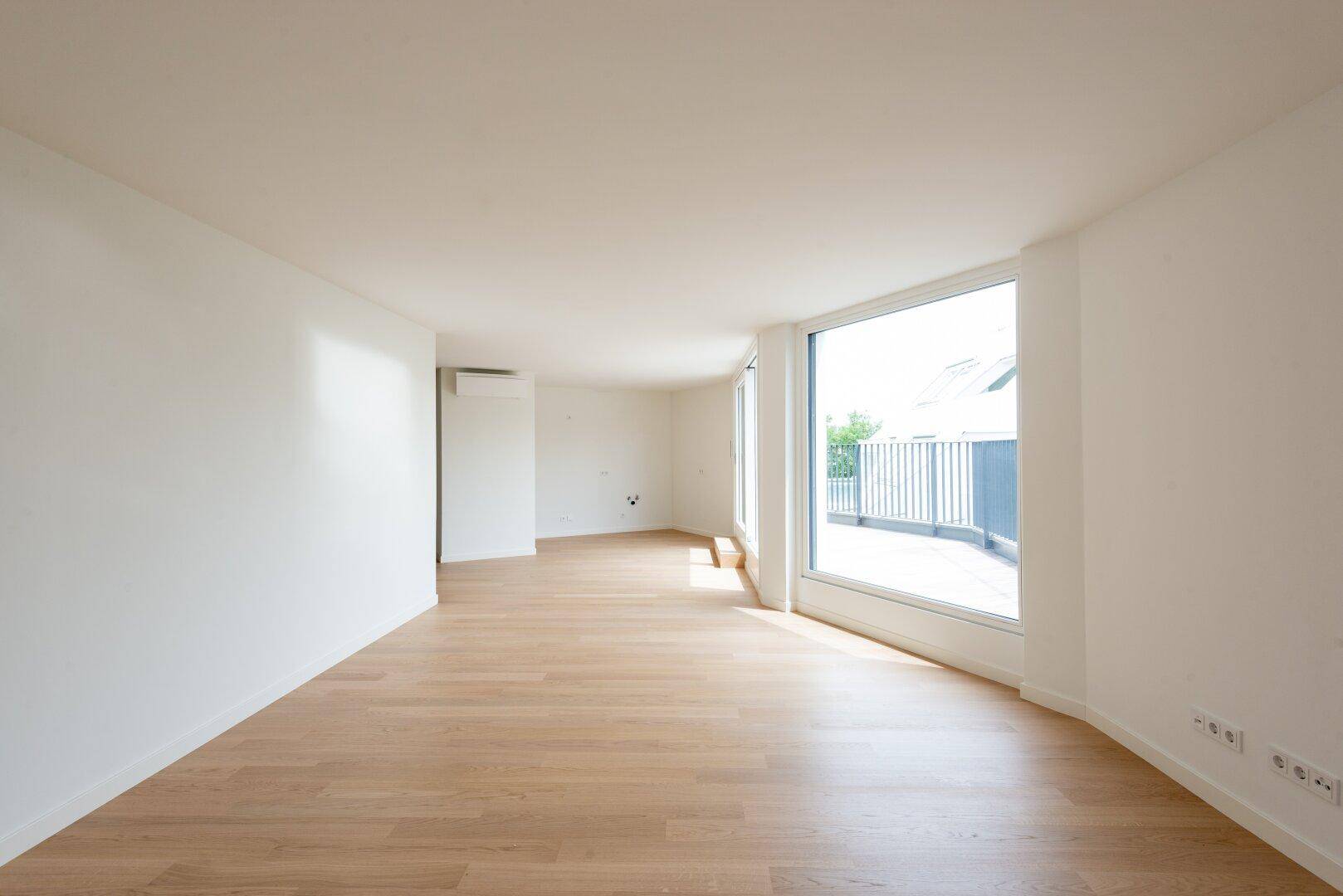Geräumiger, heller Raum mit Parkettboden, großen Fenstern und Klimaanlage.