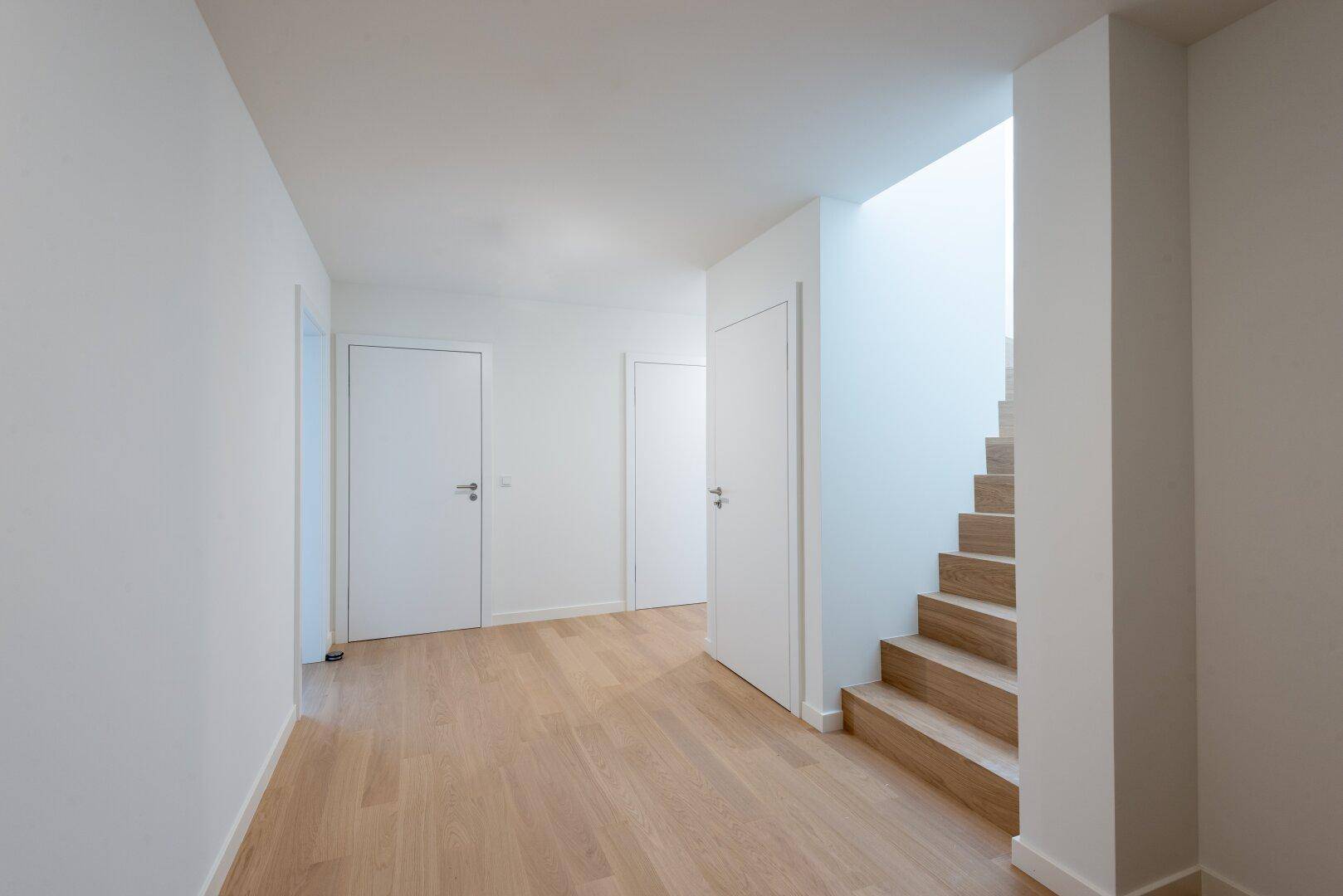 Heller Flur mit Holztreppe und hellem Holzparkettboden, der zu weiteren Räumen führt.