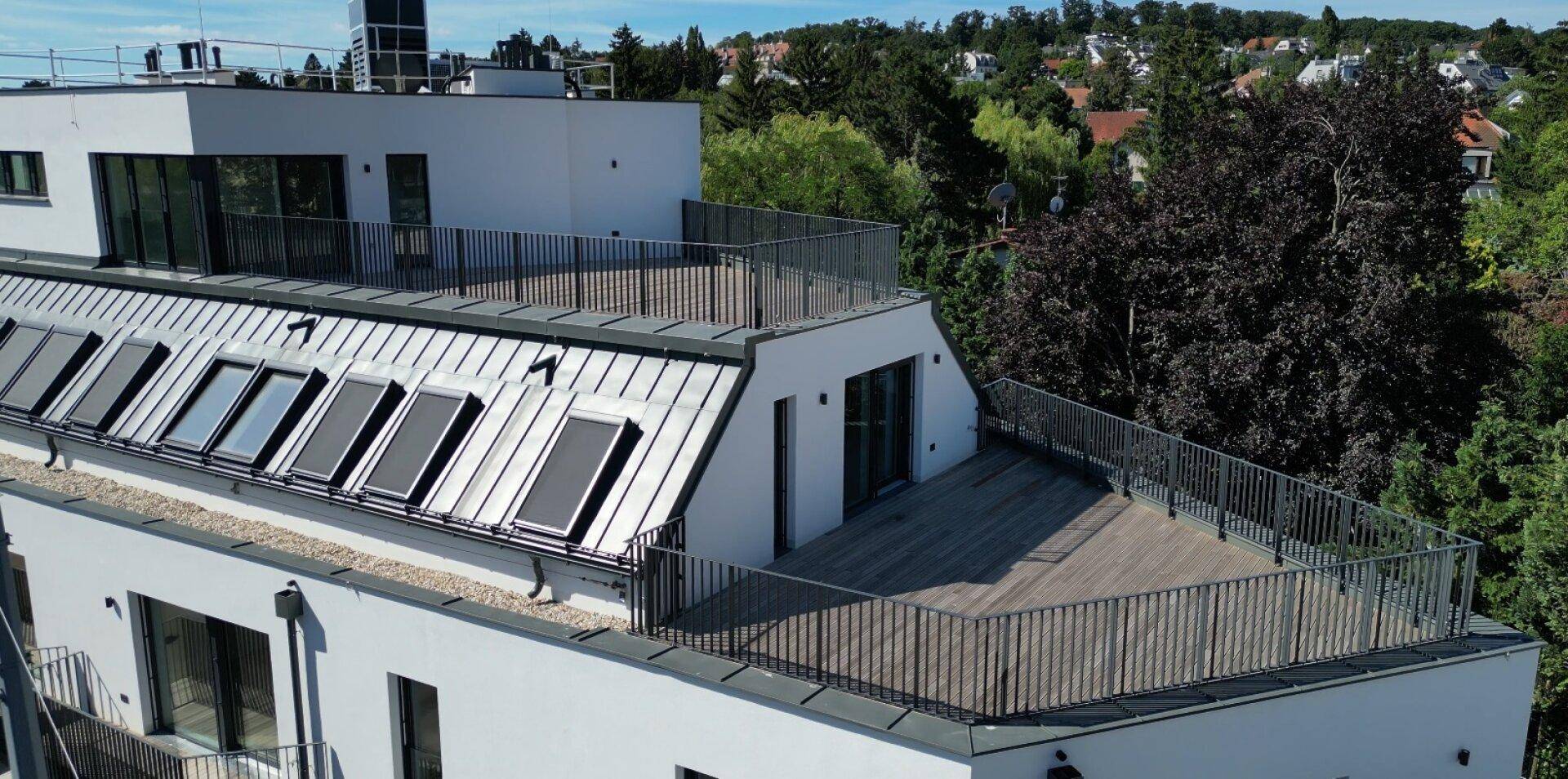 Moderne Dachgeschosswohnung mit großer Dachterrasse und weiteren Balkonen, umgeben von viel Grün.