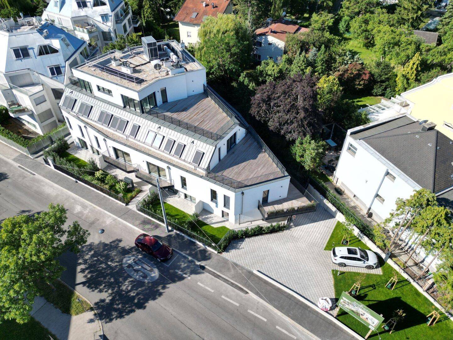 Moderne Wohnanlage mit weißer Fassade, gepflasterter Einfahrt und gepflegten Grünflächen.