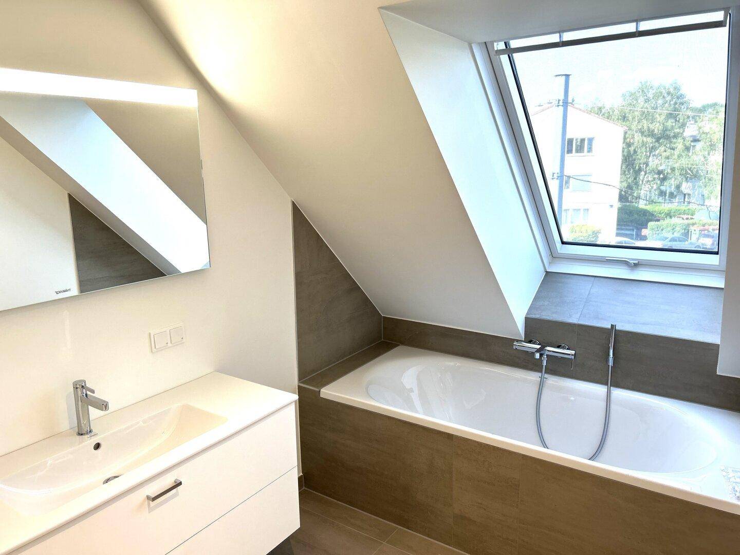 Modernes Badezimmer im Dachgeschoss mit Badewanne, Waschtisch und großem Dachfenster.