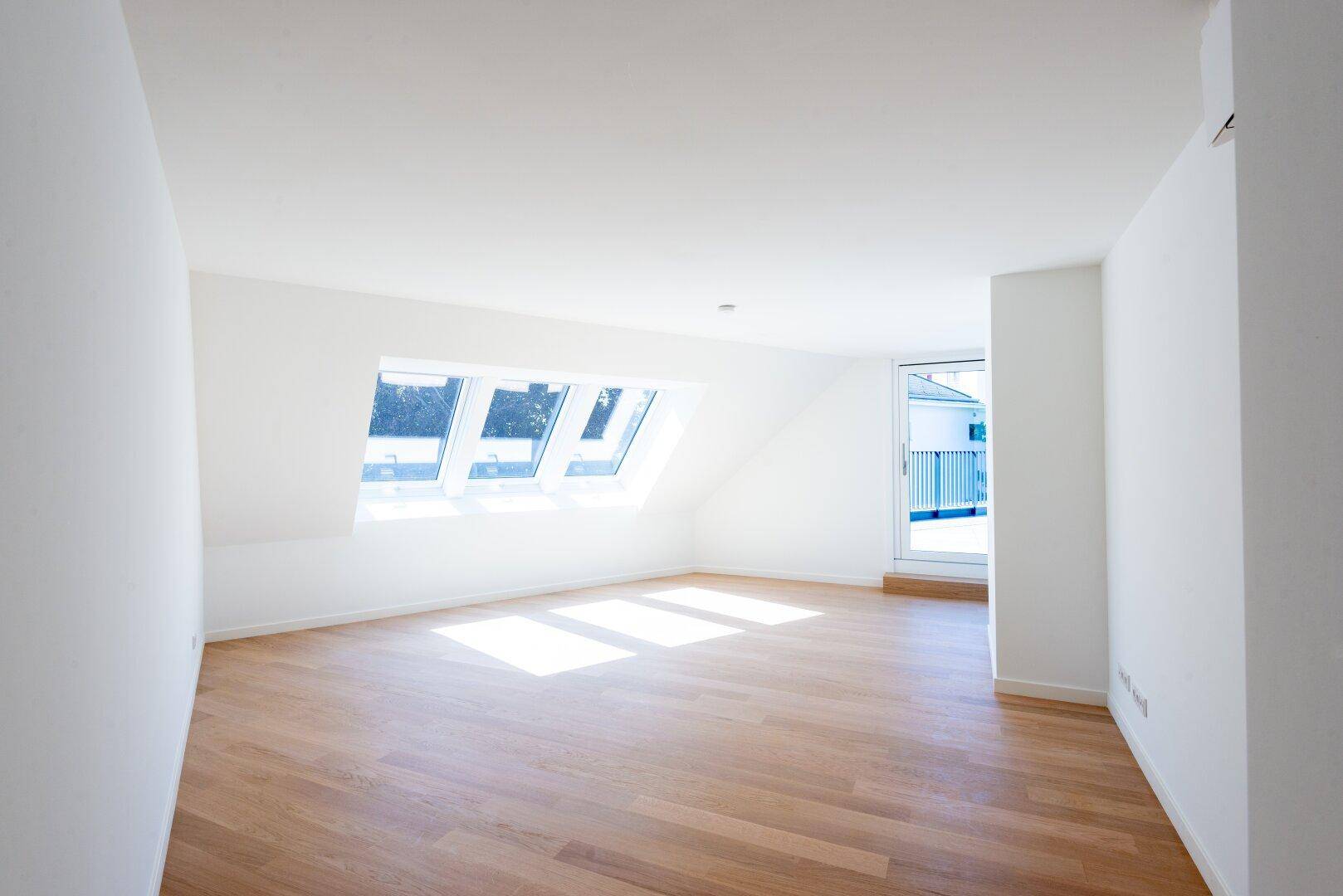 Lichtdurchfluteter Raum mit Holzboden, weißen Wänden und mehreren Dachfenstern.