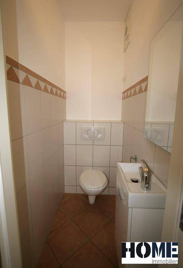 Gäste-WC mit Wand-WC, kleinem Waschbecken und Terrakotta-Fliesenboden.