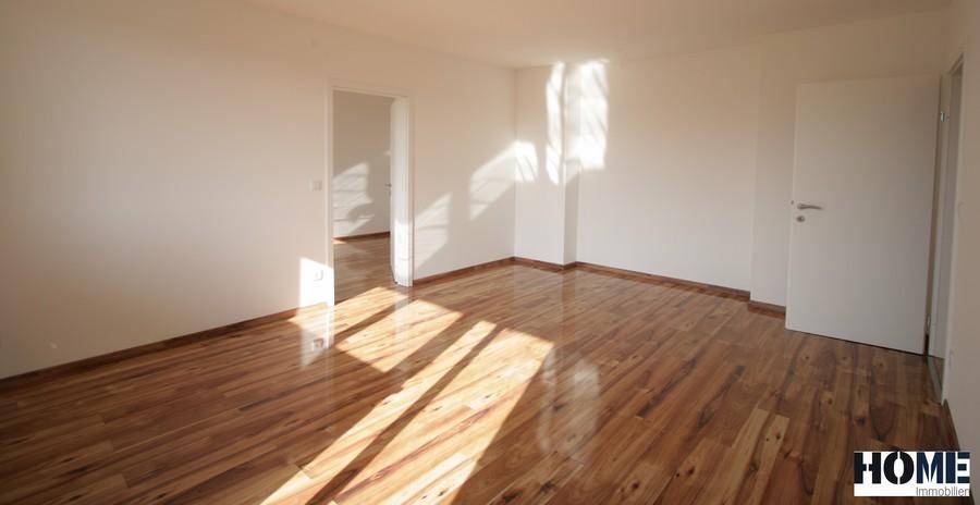 Geräumiger, heller Raum mit glänzendem Holzfußboden und weißen Wänden.