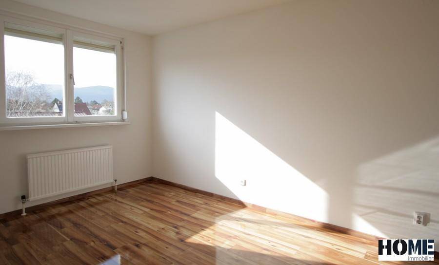 Helles Schlafzimmer mit Holzfußboden und Fenster mit Blick ins Grüne.