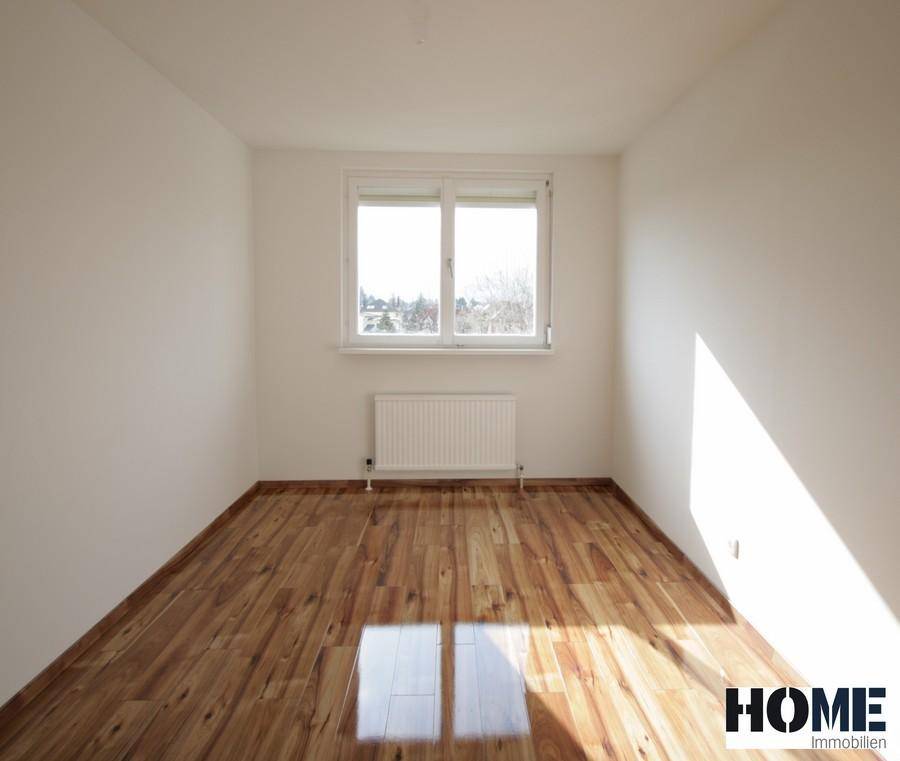 Helles Schlafzimmer mit Holzboden und großem Fenster, das den Raum mit Sonnenlicht füllt.
