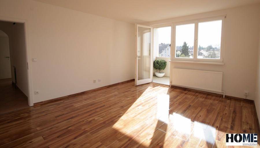 Heller Wohnraum mit Parkettboden und Zugang zu einem kleinen Balkon, der viel Licht hereinlässt.