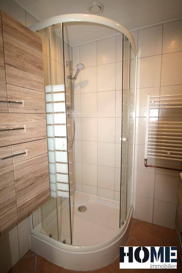 Modernes Badezimmer mit Duschkabine, weißen Fliesen und einem beheizten Handtuchhalter.