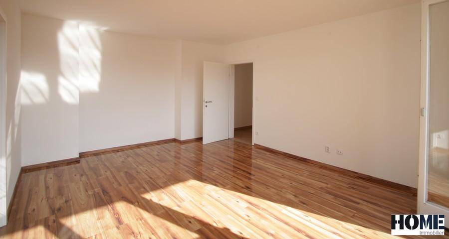 Helles, leeres Zimmer mit glänzendem Parkettboden und viel natürlichem Lichteinfall durch das Fenster.