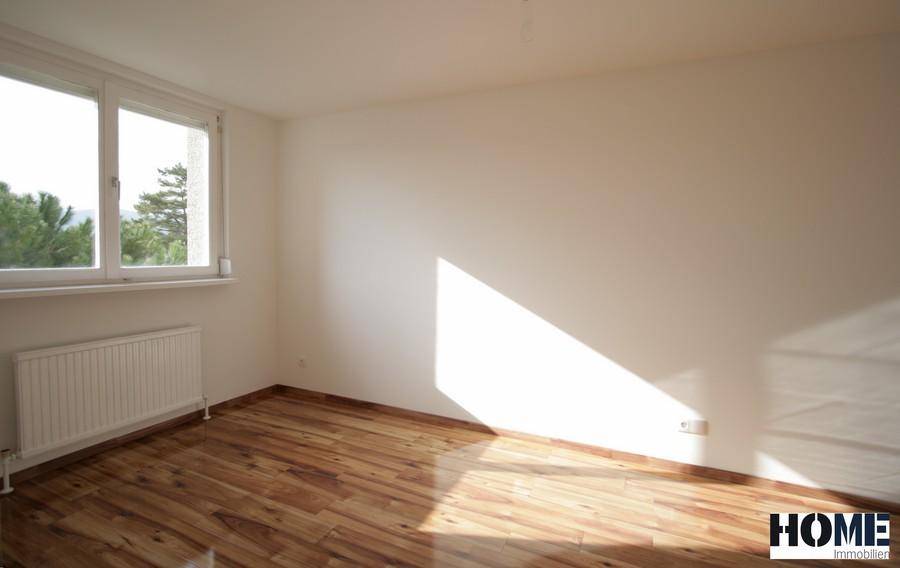 Leeres Schlafzimmer mit Holzboden, Heizkörper und Blick ins Grüne durch das Fenster.