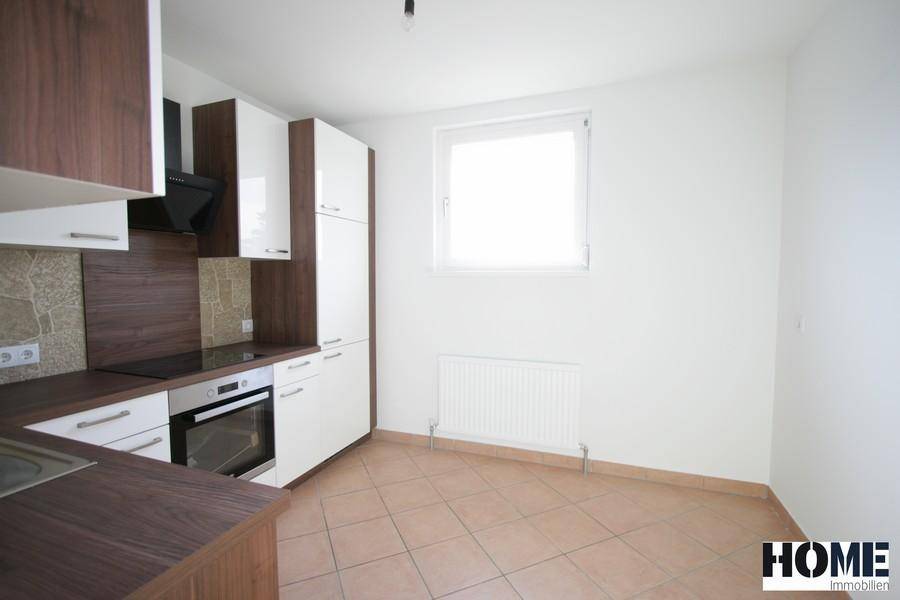Moderne Küche mit weißen und holzfarbenen Schränken, Fliesenboden und Fenster für natürliches Licht.