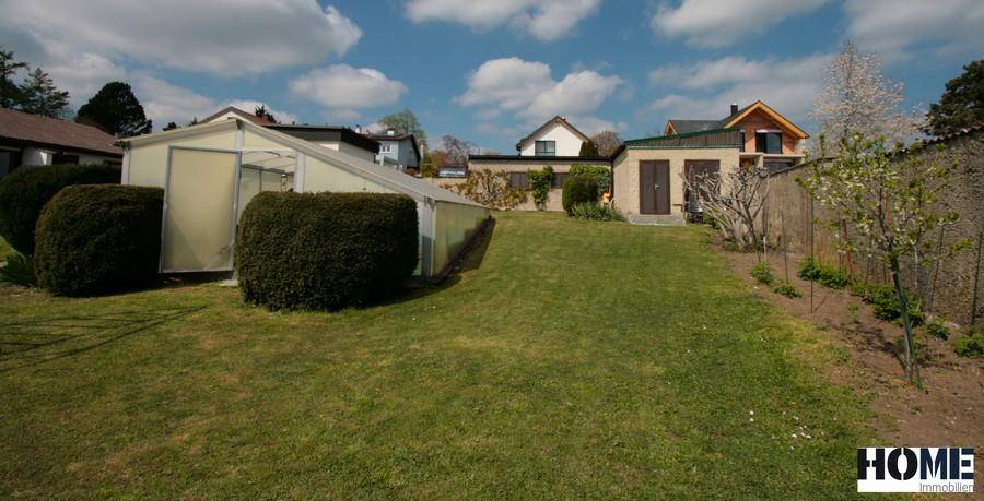 Gartenbereich mit Rasenfläche und einem Nebengebäude im Hintergrund.