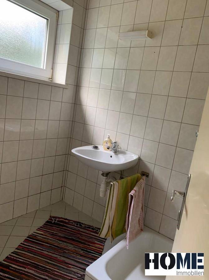 Badezimmer mit weißen Fliesen, einem Waschbecken und einer Badewanne, gut beleuchtet durch ein Fenster.