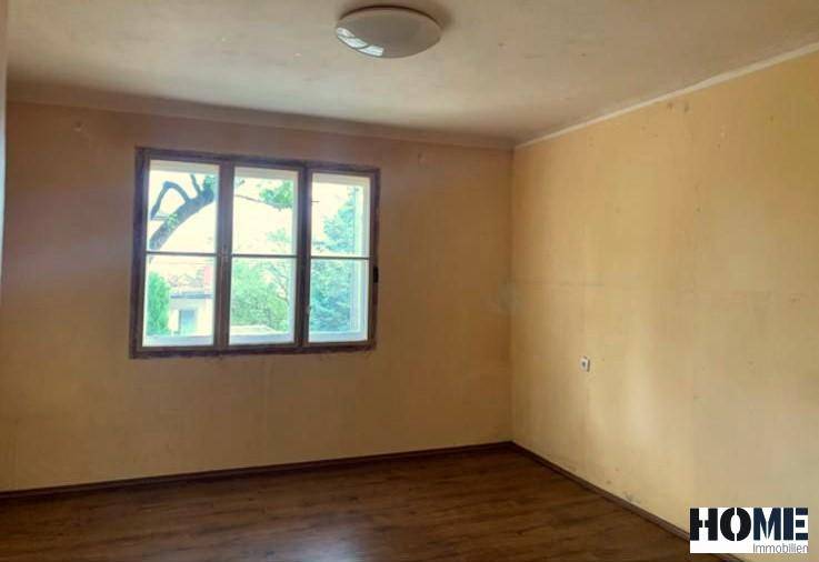 Heller, leerer Raum mit einem Fenster und dunklem Holzboden, der auf eine individuelle Gestaltung wartet.