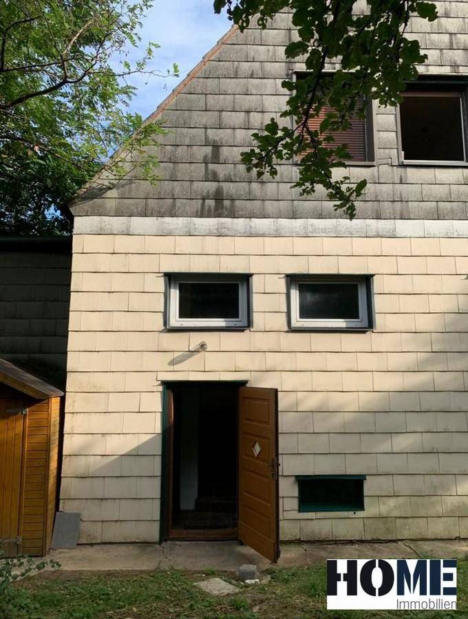 Rückseite des Hauses mit unterschiedlicher Fassadenverkleidung und einer offenen Eingangstür, die zum Garten führt.