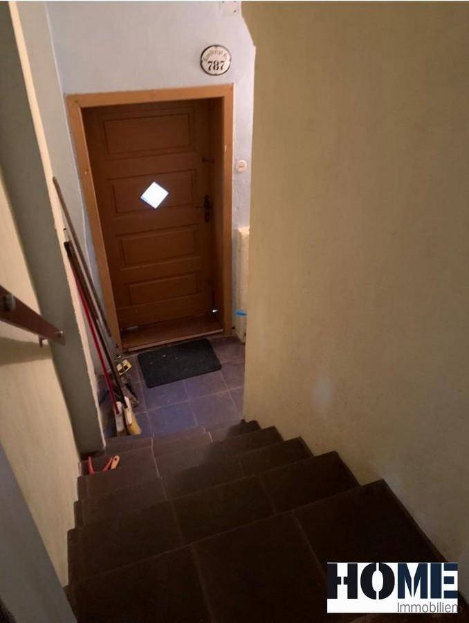 Treppenhaus mit braunen Fliesenstufen, das nach unten führt, mit einer Holztür am Ende des Flurs.