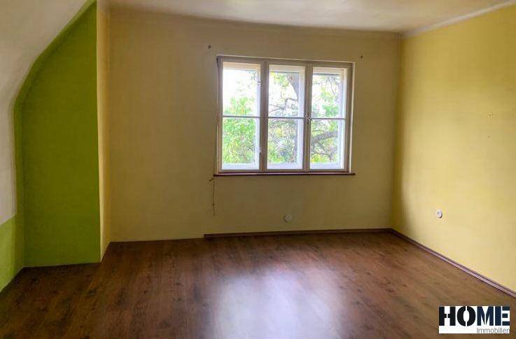 Dachzimmer mit gelben und grünen Wänden, dunklem Holzboden und einem Fenster mit Blick ins Grüne.