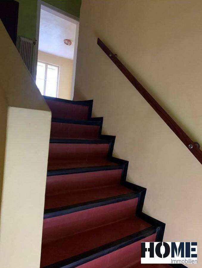 Treppenhaus mit roten Stufen und einem Holzgeländer, das in die obere Etage des Hauses führt.